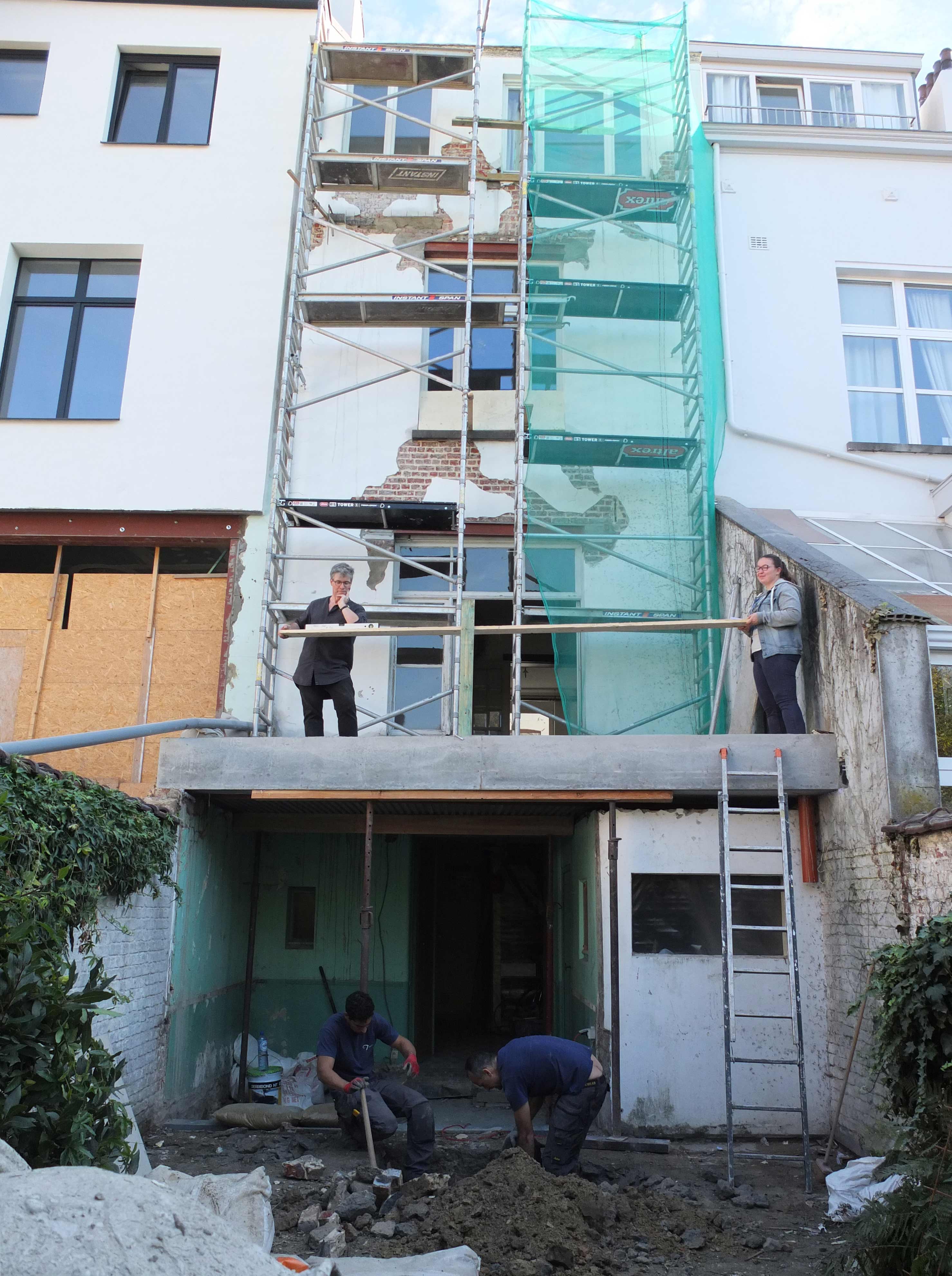 photo de chantier en cours : depuis le jardin, maître d'ouvrage et architecte font des essais de hauteur de garde-corps de la terrasse pendant que les ouvriers font le terrassement